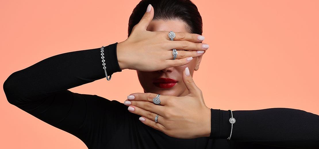 Woman wearing diamond rings and bracelets showcasing fine jewelry on hands against peach background